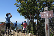 右側に大普賢岳の看板があり、景色を楽しむ参加者の写真