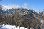 雪で白くなった和佐又山の山頂を背景に、雪が積もった地面の上を歩いている参加者の写真