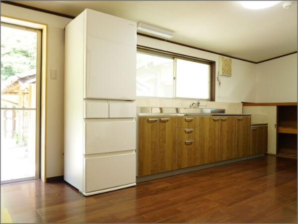 大きな白い冷蔵庫の横に木目柄のキッチンが設置された台所の写真